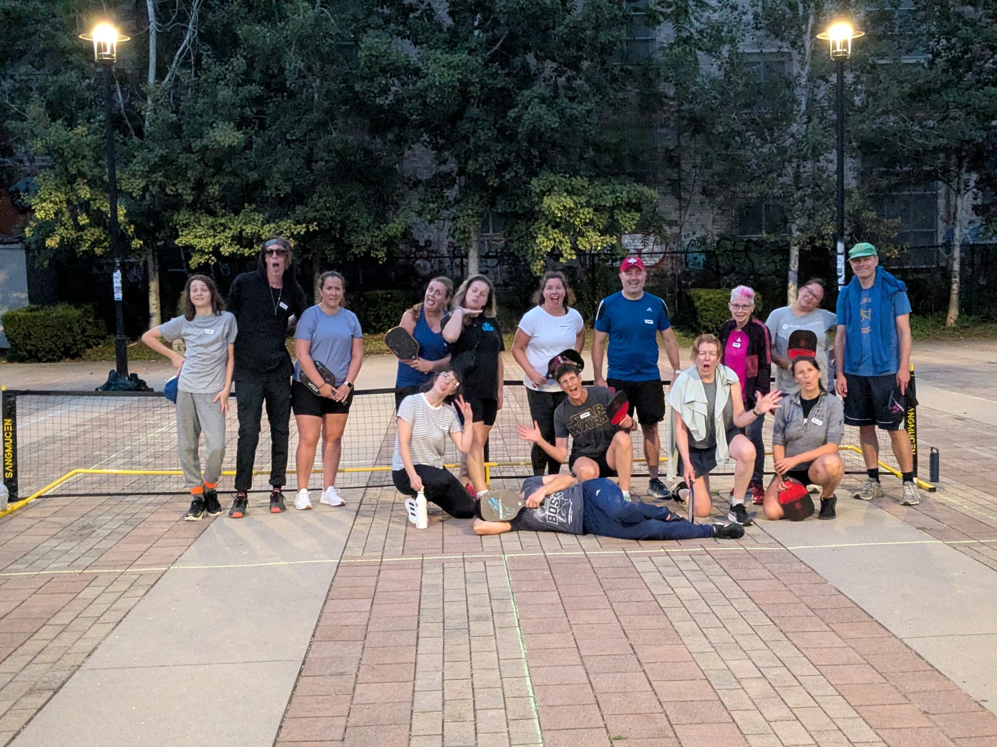 A group of neighbours of all ages posing behind a portable net on a chalk-lined court at Sorauren Park