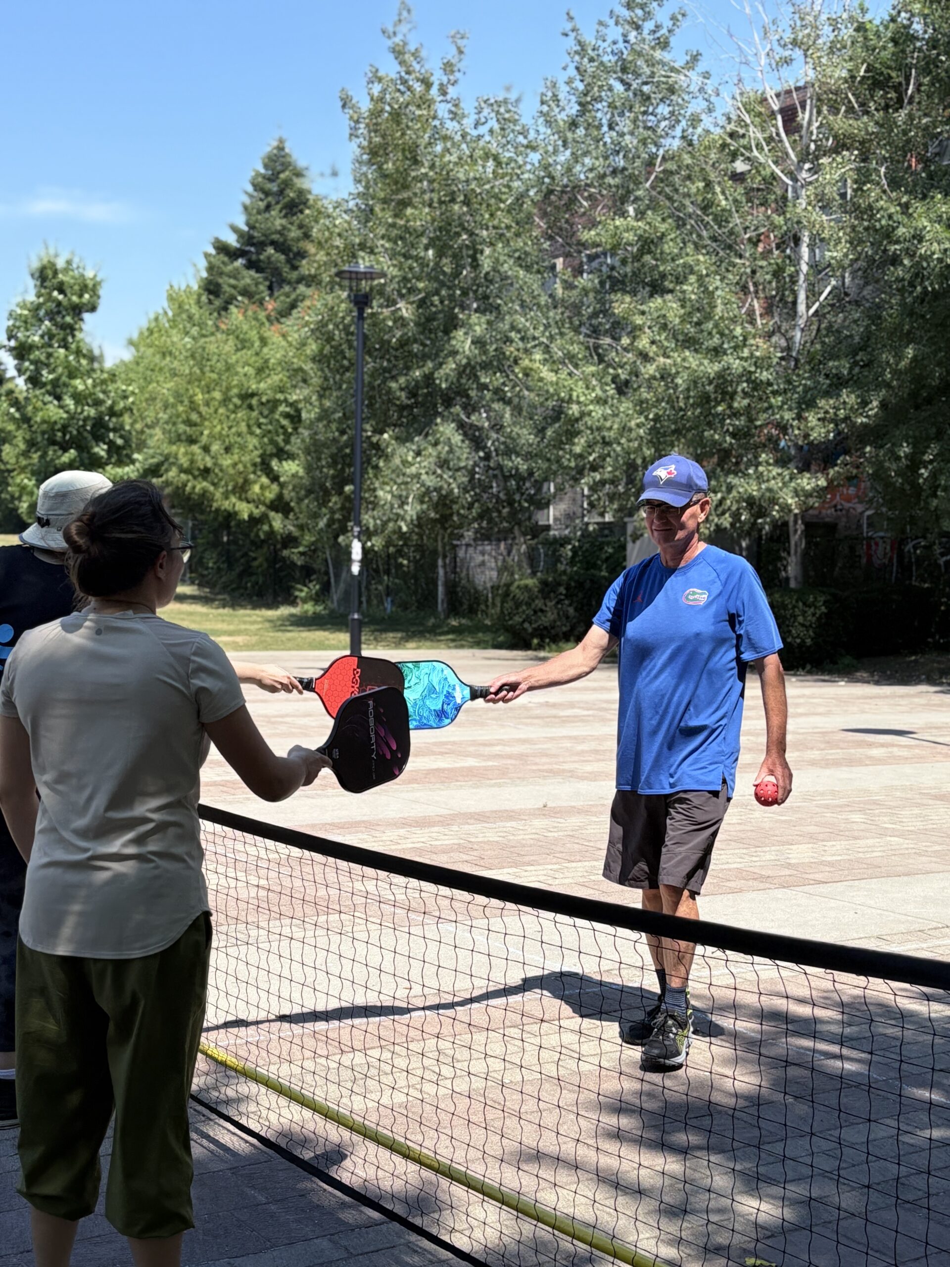One player passing a pickleball paddle to another across the net at Sorauren Park